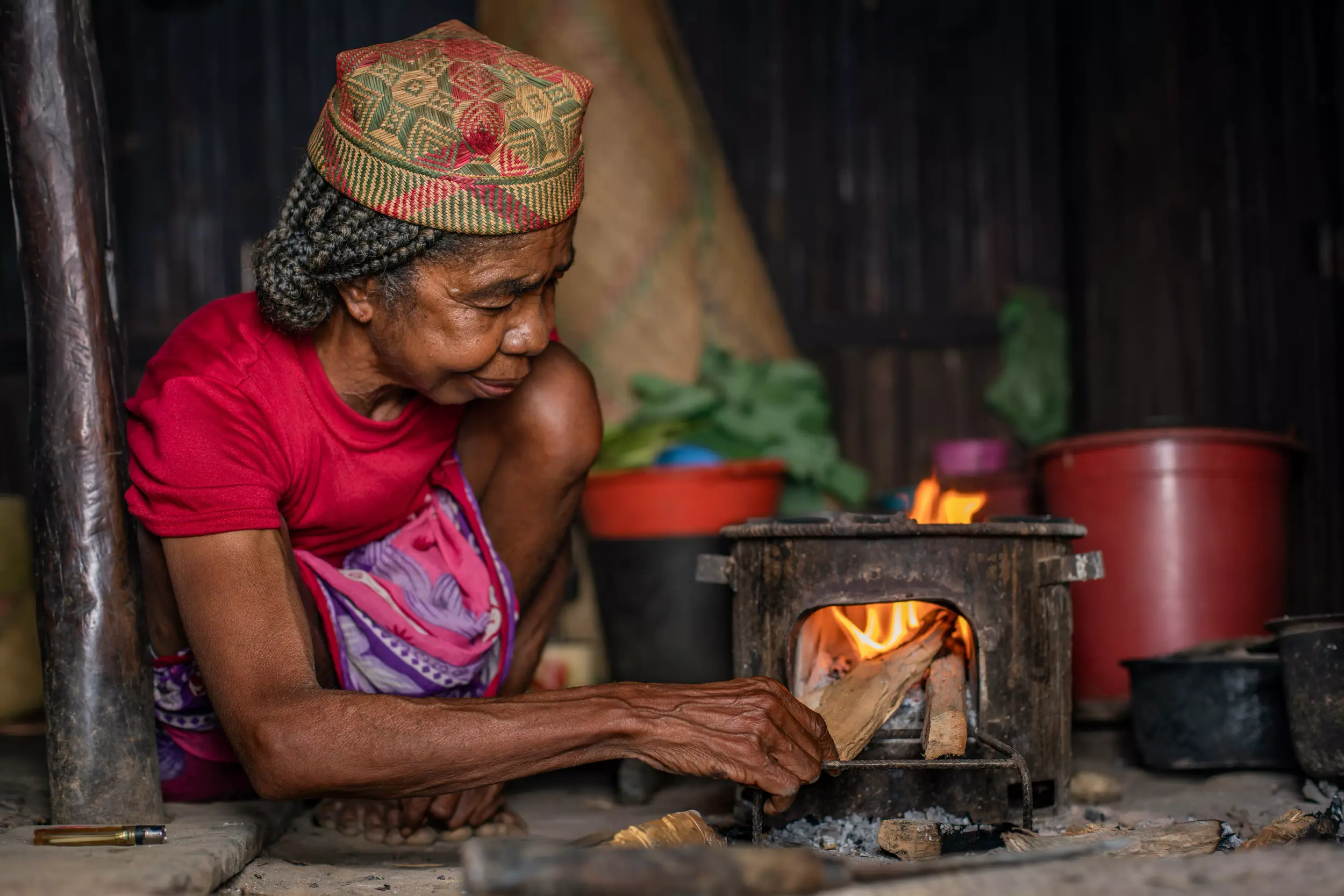 Elderly woman putting wood in portable cookstove